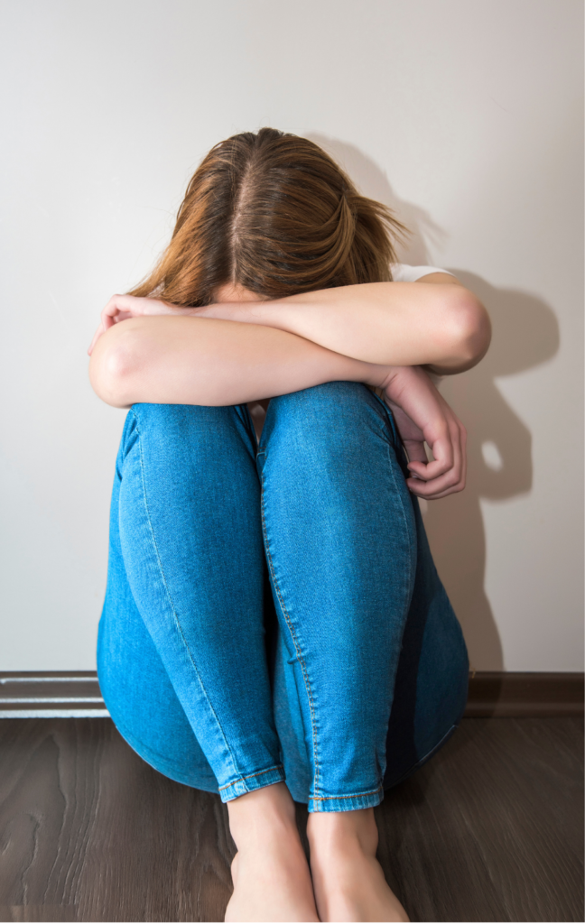 Mulher sentada no chão, abraçando os joelhos, representando ansiedade e sofrimento emocional